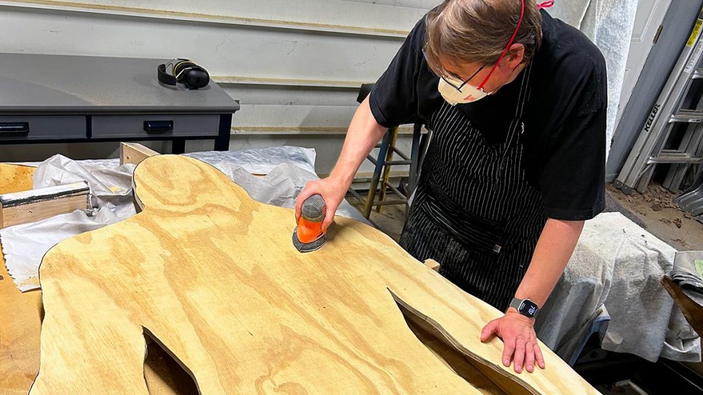 A person sanding a large Bigfoot cutout.