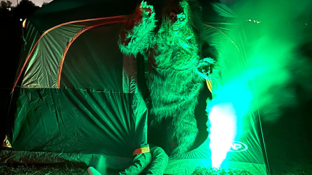 Bigfoot coming out of a tent at night through a column of green fog.