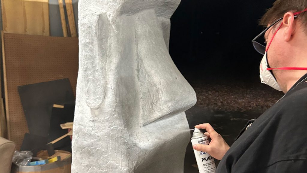 A person using a spray can to paint a moai statue.