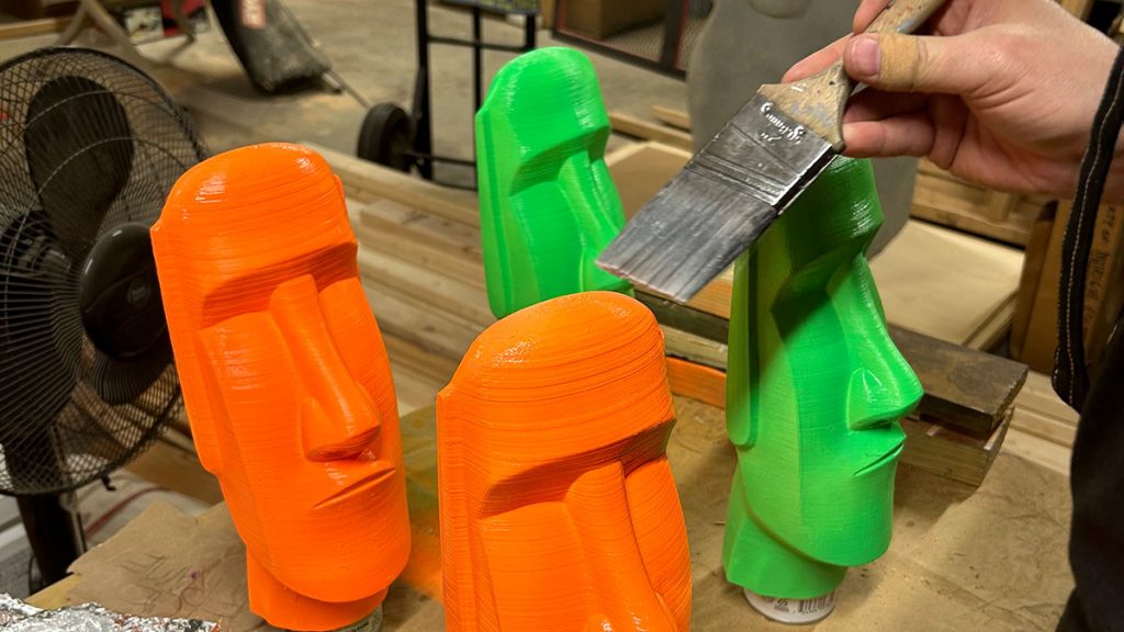 A hand painting some colorful moai statues.