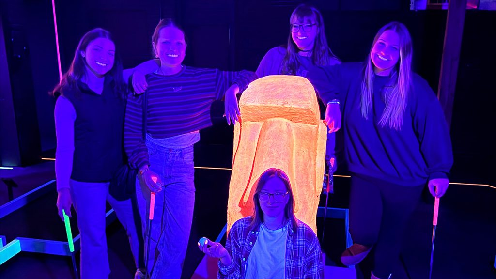 Happy players posing in front of an orange moai statue.