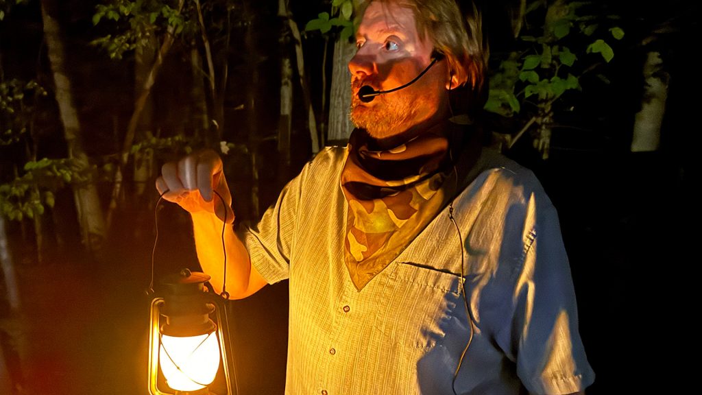A tour guide deep in the woods holding a lantern